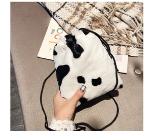 Detail of soft plush crossbody bag featuring black and white cow print with drawstring closure