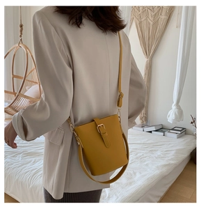 Detail of a bright yellow bucket bag with matte leather texture and adjustable strap