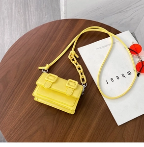 Detail of yellow mini crossbody bag with leather texture and chain strap on wood