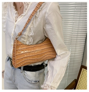 Detail showing a light brown crocodile texture baguette bag worn on a woman's shoulder