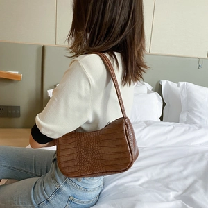 Sac sous le bras marron foncé à motif crocodile porté par un mannequin chez soi