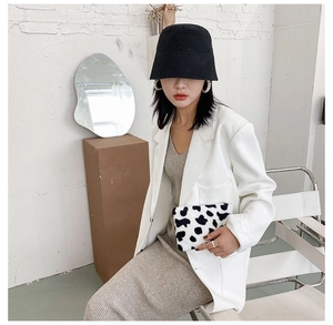 Pochette en peluche à motif vache portée avec un costume blanc et un bob noir élégant