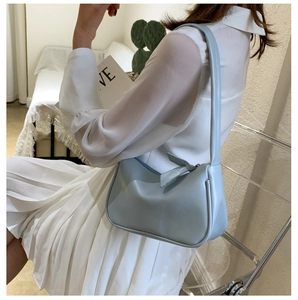 Close-up of light blue leather underarm bag featuring minimalist curves and zipper