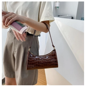 Detail of dark brown croc-effect baguette bag with glossy finish and gold zipper