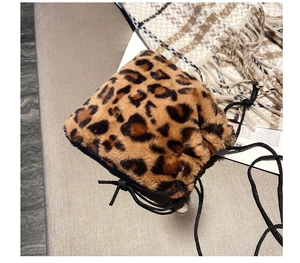 Close-up of leopard print faux fur bucket bag with black drawstrings on stone surface