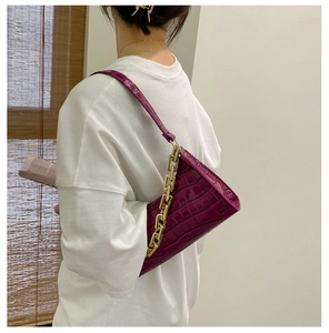 Detail of purple crocodile pattern shoulder bag with a gold chain strap on model