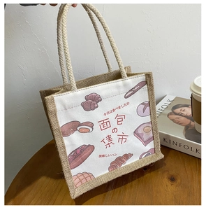 Detail of canvas jute tote bag featuring bread illustrations and woven handles on a desk