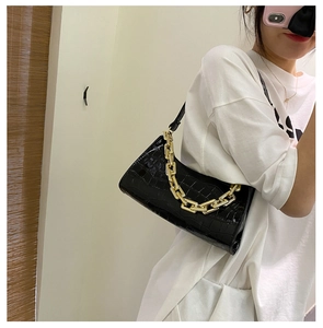 Side view of a black crocodile pattern underarm bag with decorative gold metal chain