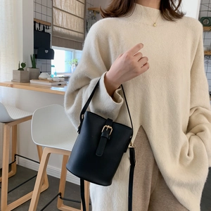 Minimalist black bucket bag with gold metal buckle and slender leather shoulder strap