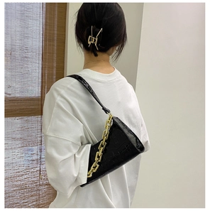 Detail of black crocodile pattern shoulder bag with a bold gold chunky chain strap