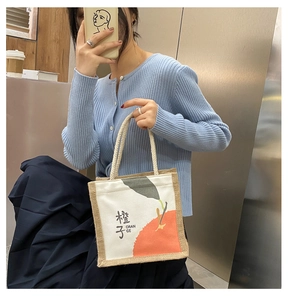 Detail of small canvas tote bag with orange print and woven rope handle held by model