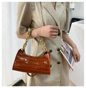 Detail view of brown crocodile embossed bag with chunky gold chain strap on shoulder