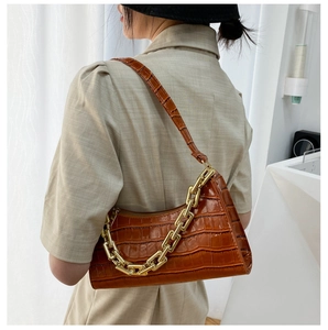 Brown crocodile pattern baguette bag with a chunky gold chain strap shown on a model