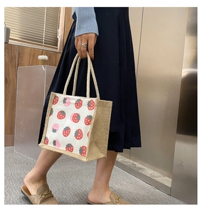 Detail view of canvas tote bag featuring strawberry print and natural jute side panels