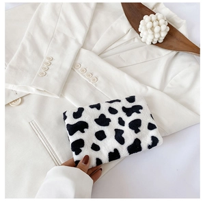 Vue détaillée du porte-monnaie en peluche motif vache sur fond blazer blanc et décoratif