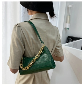 Detail view of deep green crocodile embossed leather bag with golden metal chain strap