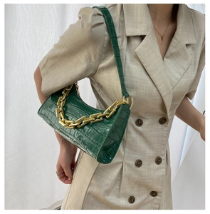 Detail of dark green crocodile texture underarm bag with decorative gold chain strap