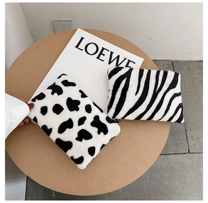 Détail de porte-monnaie en peluche aux motifs vache et zèbre sur un plateau en bois