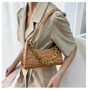 Brown crocodile-textured underarm bag with thick gold chain worn on beige blazer