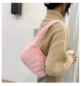 Side view of model wearing pink plush faux fur underarm bag with minimalist sweater