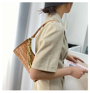Detail view of brown crocodile pattern shoulder bag with a bold gold chain on a female model