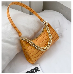 Macro view of a yellow crocodile-embossed underarm bag with a chunky gold chain