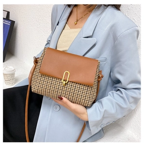 Close-up of stylish retro houndstooth crossbody bag with brown leather flap and golden buckle