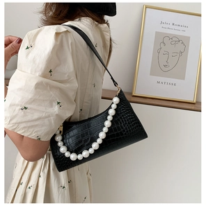 Detail view of black crocodile pattern underarm bag with decorative white pearl strap