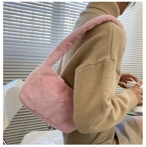 Detail of pink plush faux fur underarm bag worn by model in a cozy indoor setting