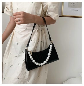 Detail of black crocodile texture shoulder bag with large white pearl strap on model