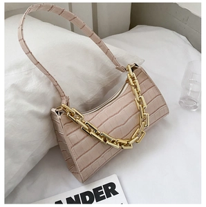 Detail of pink crocodile embossed leather bag with chunky gold chain strap on white bed