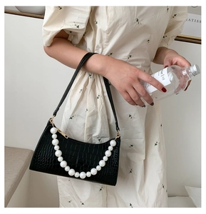 Close-up of black faux crocodile leather underarm bag with large pearl chain details