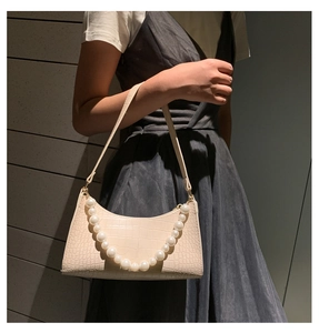 Detail of cream baguette bag featuring embossed faux crocodile leather and large pearls