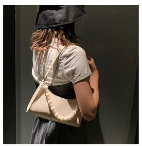 Close-up of cream underarm bag with crocodile texture and large pearl chain detail