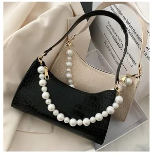 Detail of crocodile-embossed baguette bags in black and beige with luxury pearl handles