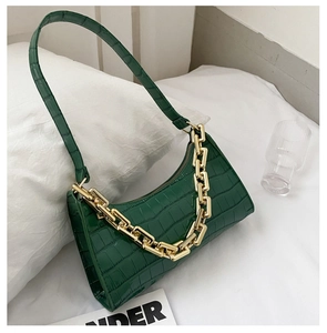 Detail view of dark green croc-effect bag with a bold gold chain on a white pillow
