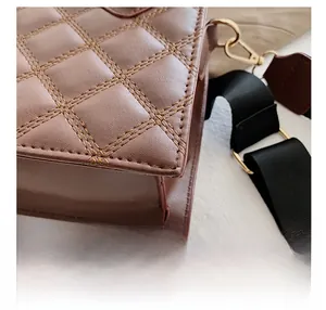 Close-up of quilted stitching and gold hook on a brown crossbody bag with black strap