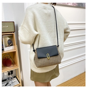 Detail view of a vintage plaid crossbody bag with a gold buckle and black leather flap