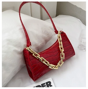 Detail of red croc-embossed underarm bag with bold gold chain on white background