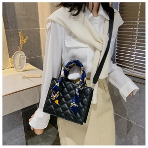 Close-up of black quilted handbag with silk scarf handle and wide textile strap