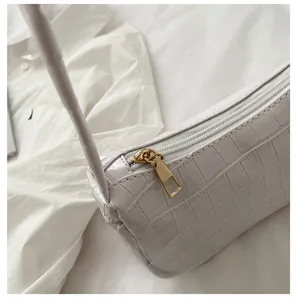Detailed close-up of golden zipper pull on a white crocodile embossed shoulder bag