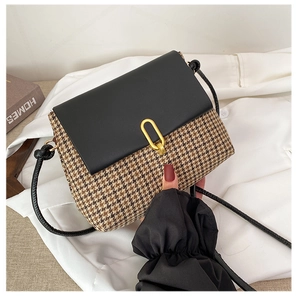 Detailed view of houndstooth crossbody bag with golden U-shaped buckle on white fabric