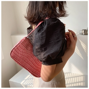 Detail of burgundy crocodile-textured shoulder bag with natural window light shadows