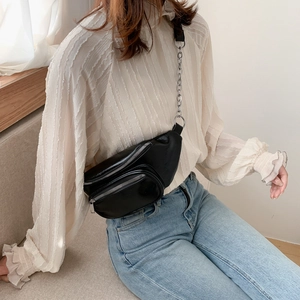 Sac banane tendance en cuir noir avec bandoulière en chaîne argentée porté par un modèle