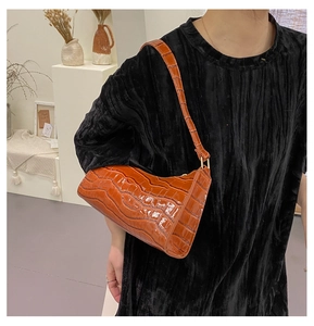 Bolso baguette marrón con grabado de cocodrilo y correa para el hombro sobre un vestido negro