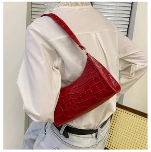 Detalle de un bolso baguette rojo con estampado de cocodrilo llevado por una modelo