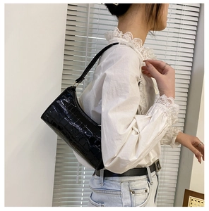 Detalle del bolso hobo negro con textura de cocodrilo con acabado brillante y asa de cadena