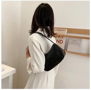 Detail of black faux crocodile leather shoulder bag shown on model in minimalist setting