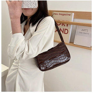 Close-up of a dark brown crocodile texture baguette bag worn by a model in a cozy setting