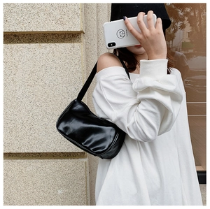 Close-up of minimalist black synthetic leather underarm bag worn on shoulder